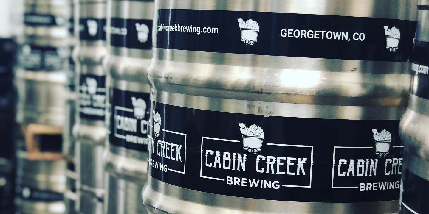 lines of kegs with black stickers that say cabin creek brewing