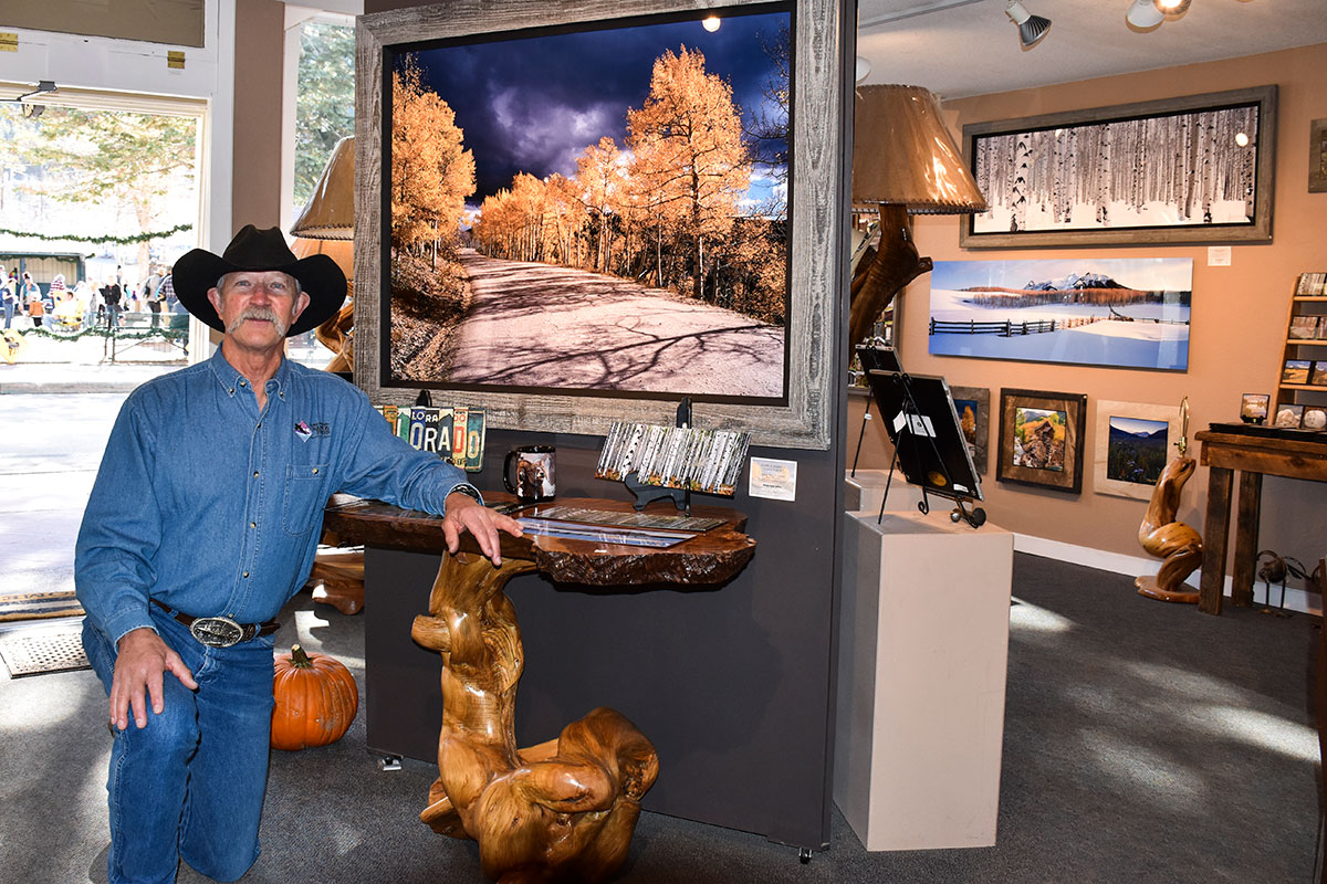 Gallery owner in western attire proudly stands in front of his collection.