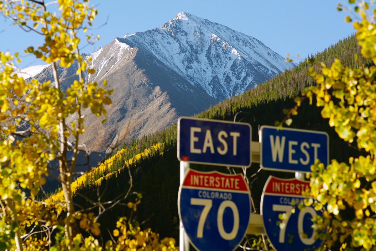Interstate road signs foreground a high mountain peak.