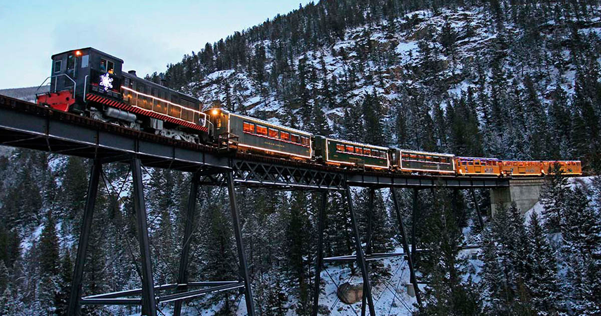 Historic holiday train travels a bridge far above the snowy ground below.