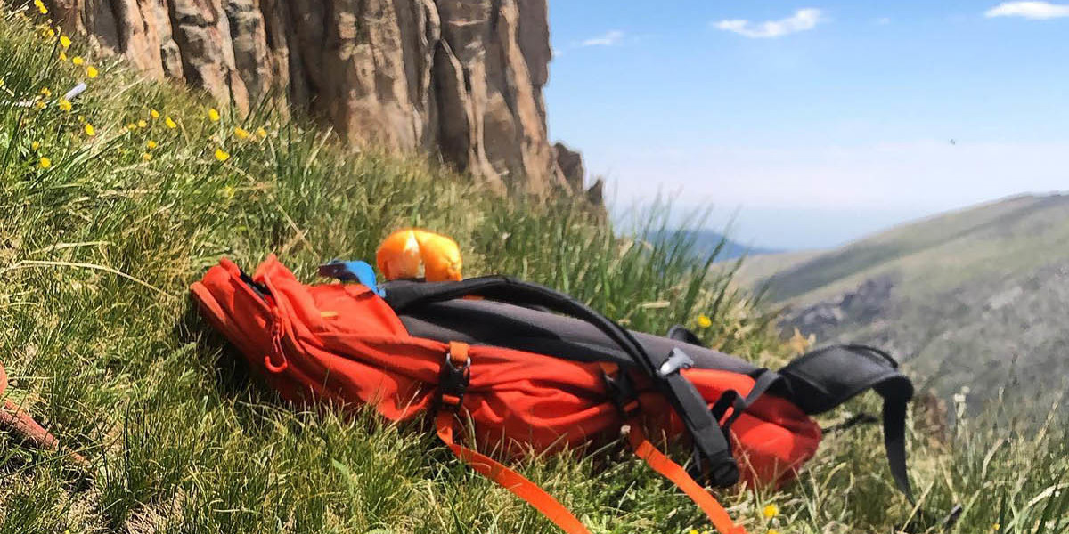 Hiking equipment laying in grass in front of a rock wall
