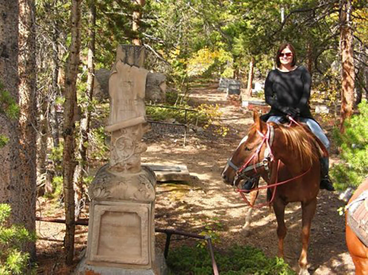 Smiling horseback rider poses next to a historic gravestone.