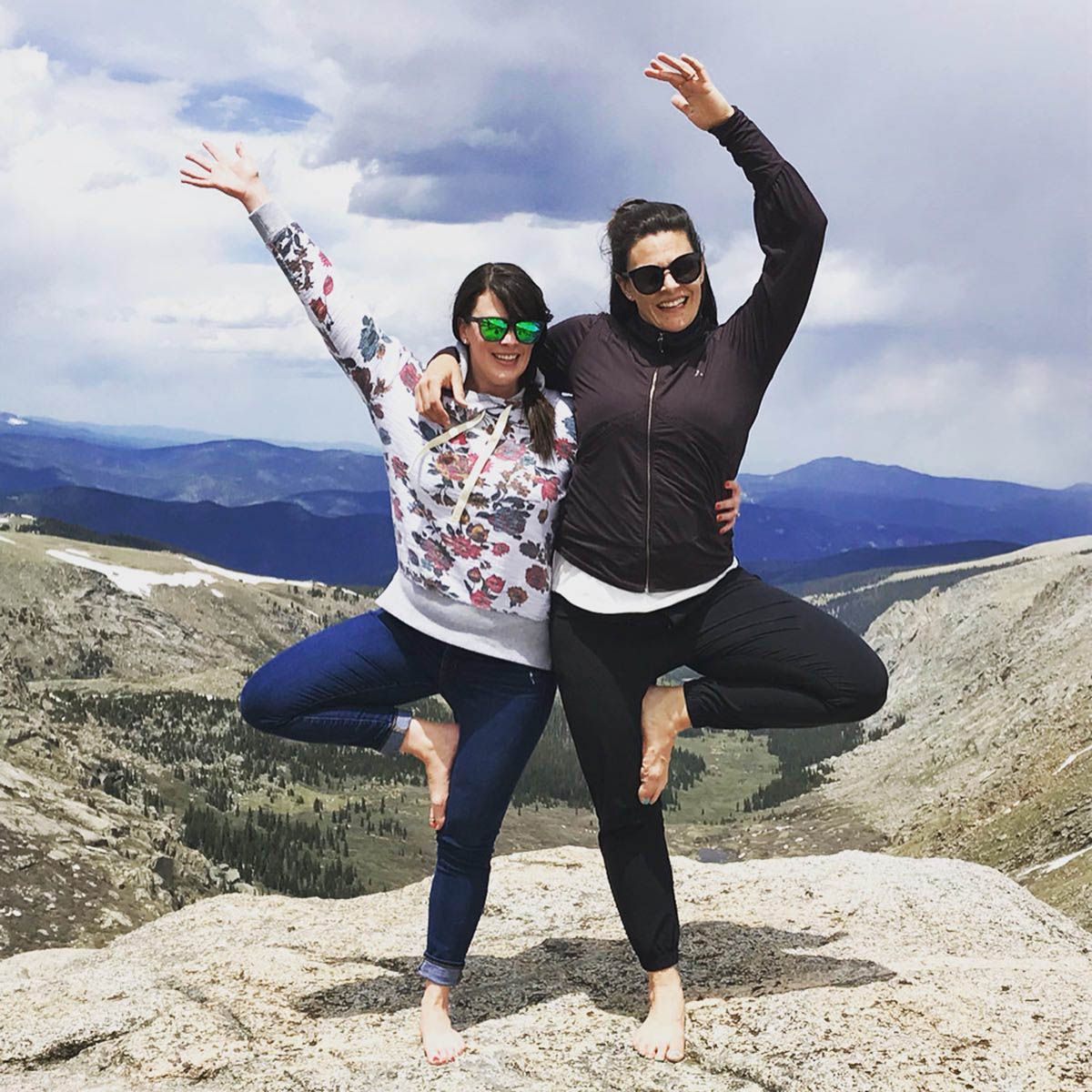 Two friends strike an elevated yoga pose on a mountain top.