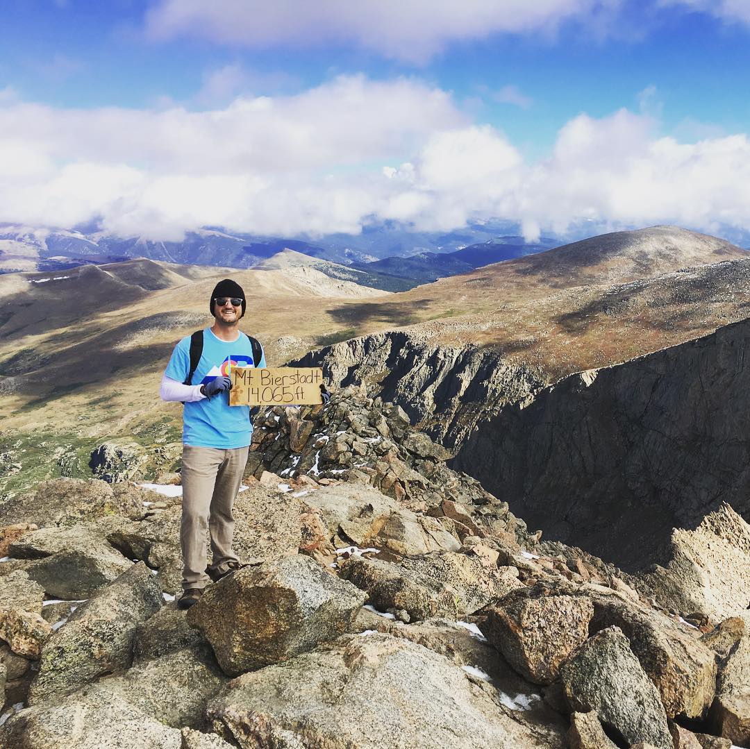 man on top of mount bierdstadt holding cardboard sign with elevation