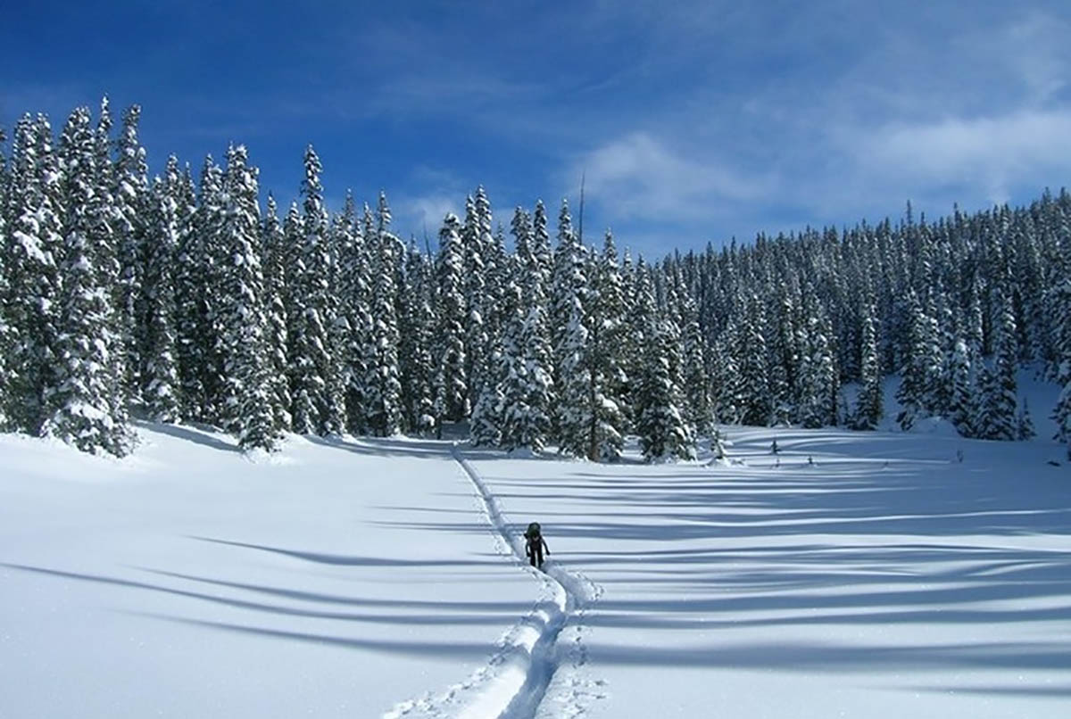 Person traverses a narrow trail through a snow-covered mountain valley.