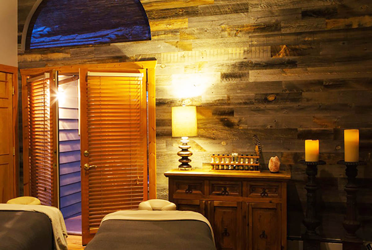 Interior of relaxing spa room with two massage tables and a wood wall.